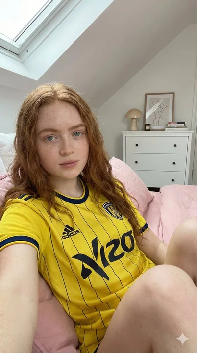 A red-haired girl in a yellow and blue jersey in the sunny attic