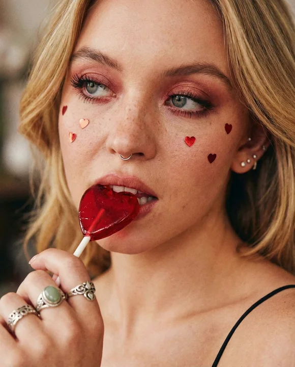 頬が赤く染まった少女がハート型のキャンディーをかじっている