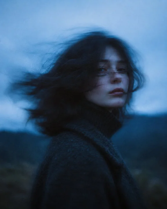 A cinematic portrait of a woman with long hair blowing in the wind at dusk
