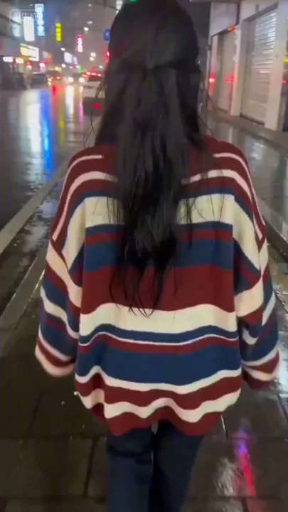 A girl with a sweet smile looking back at the camera on a rainy night, neon-lit streets, holding a lens.
