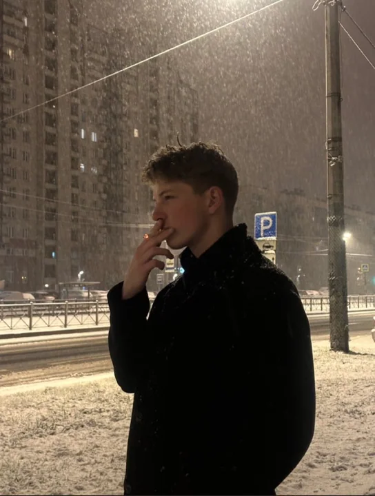 Унылое профильное лицо, курящее под уличным фонарем в снежную зимнюю ночь