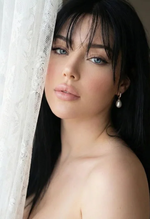 A stunning close-up of a black-haired girl with blue eyes under lace-patterned light and shadow