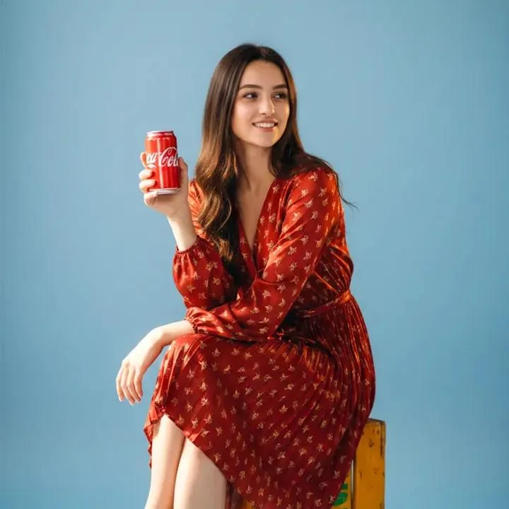 A fun moment of a girl in a red dress raising a cola, viewed from a fish-eye perspective.